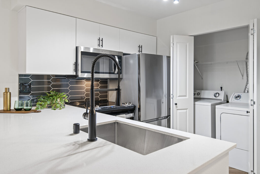 A kitchen with a stainless steel sink, refrigerator, and microwave. There are also cabinets and drawers for storage.
