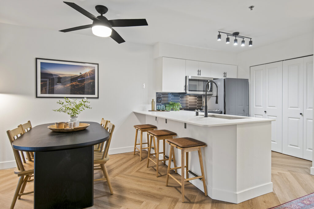 A kitchen and dining area with a ceiling fan. The kitchen has stainless steel appliances and granite countertops. There is a table with four chairs in the dining area.
