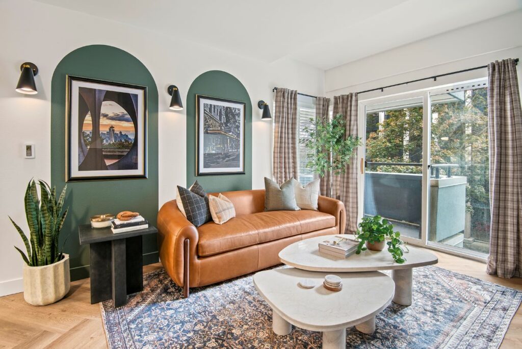 A living room with a modern couch and a glass coffee table. There is a sliding glass door in the background leading to a balcony.